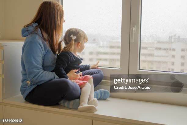 mother and daughter looking out of the bedroom window on a rainy day - criança stock pictures, royalty-free photos & images