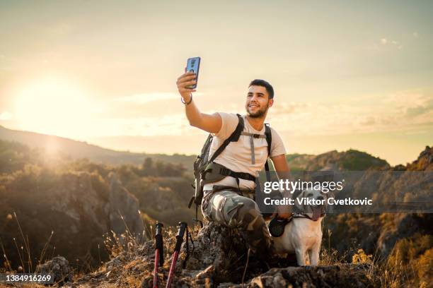young man taking selfies with sunset while on a break from hiking - hiking pole stock pictures, royalty-free photos & images
