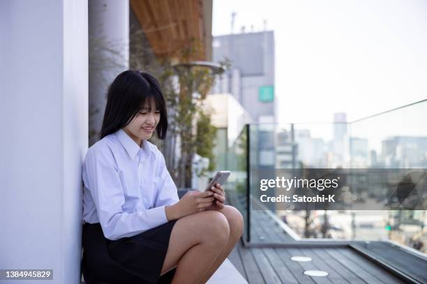 teenage girl sitting on rooftop and using smart phone - smiling - female high school student stock pictures, royalty-free photos & images