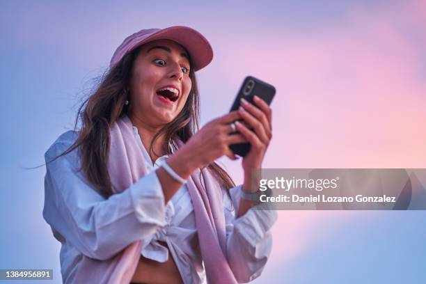 excited woman using smartphone at sunset - surprise fotografías e imágenes de stock
