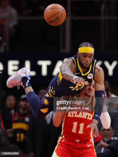 Oshae Brissett of the Indiana Pacers is charged with a foul as he falls over the back of Trae Young of the Atlanta Hawks battling for a reboundduring...