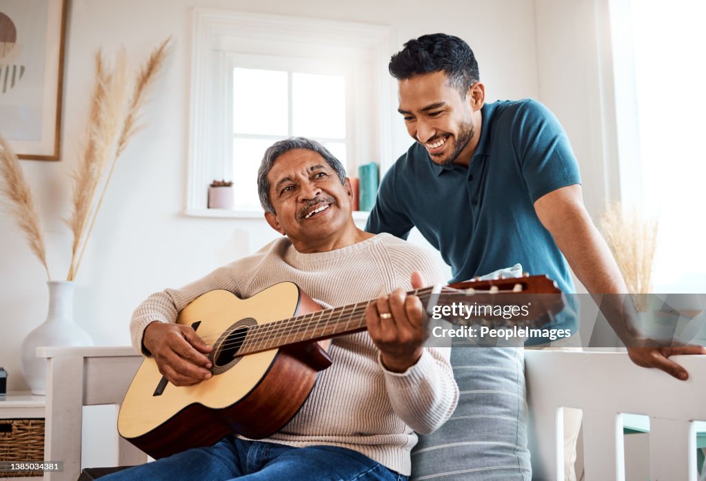 Shot of a young man listening to his father play the guitar at home