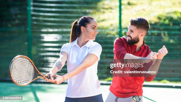 tennis instructor giving lessons to young woman in tennis court - tennis adult stock pictures, royalty-free photos & images