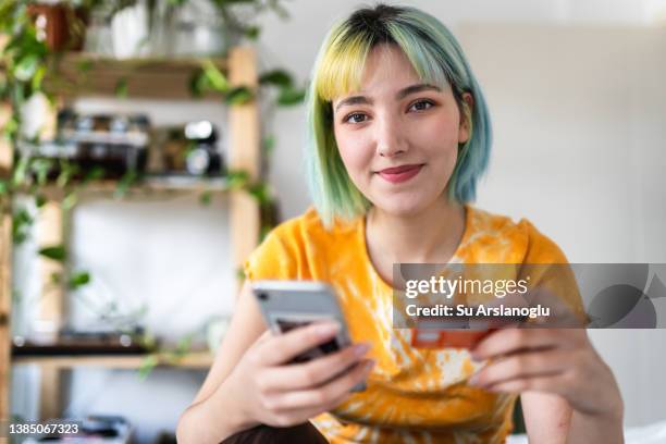 giovane donna con i capelli colorati sta acquistando online con una carta di credito - looking at camera foto e immagini stock