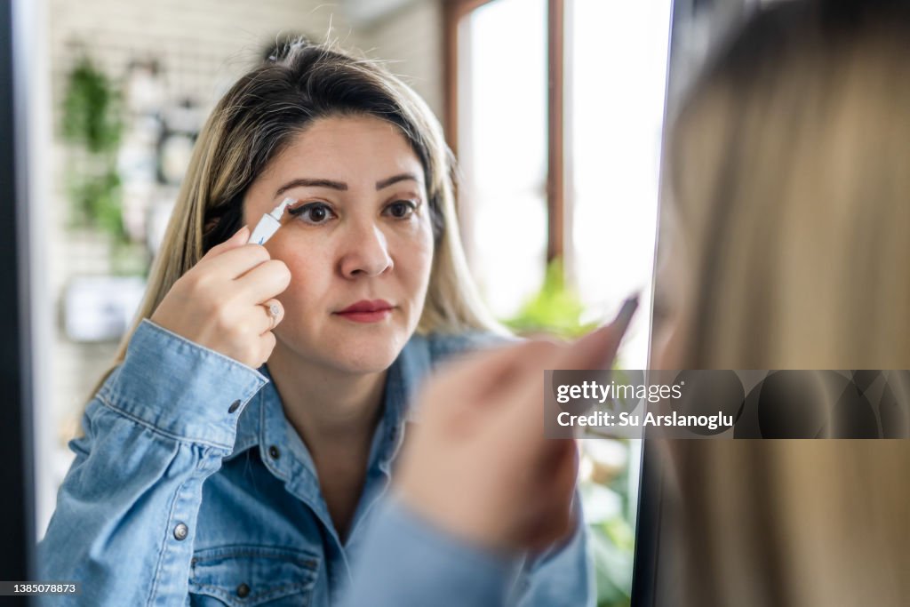 Woman having eyelid surgery applies eye cream at home