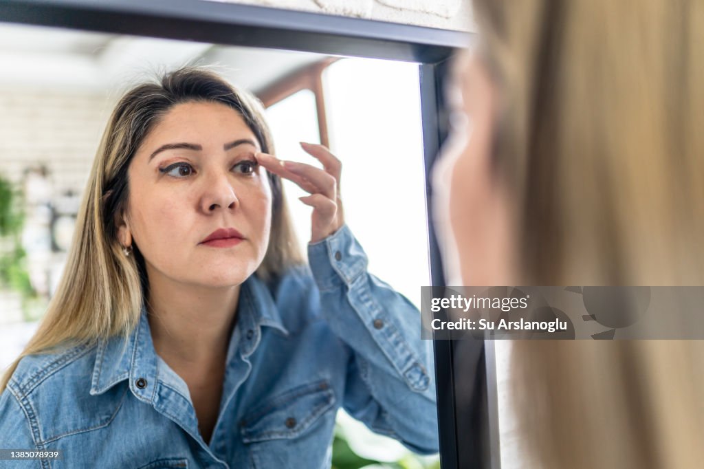 Woman having eyelid surgery applies eye cream at home