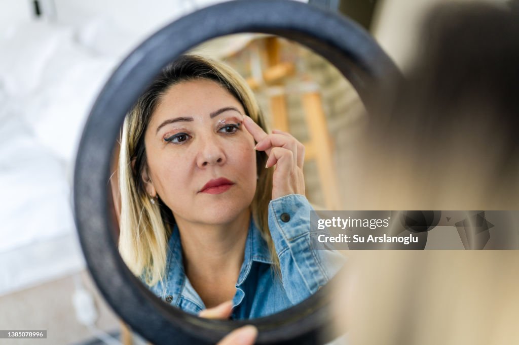 Woman having eyelid surgery applies eye cream at home