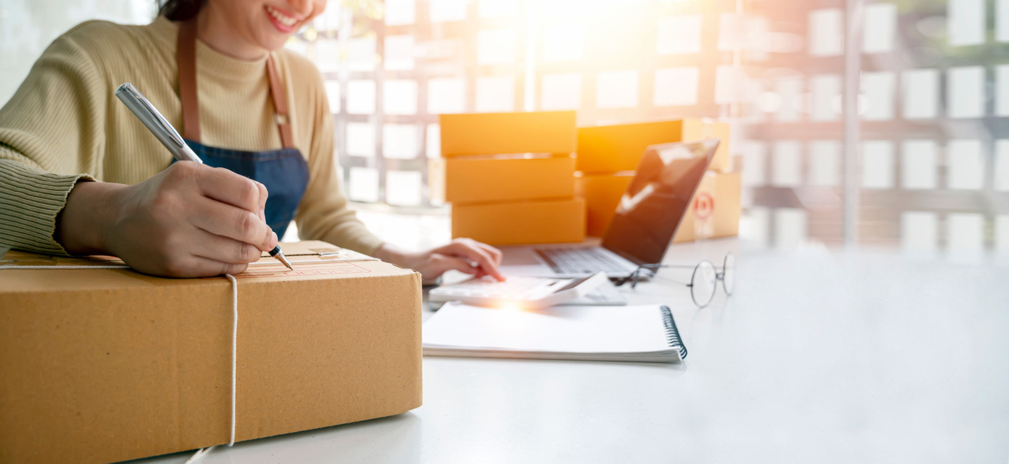 Young woman small business owner writing on parcel box preparing package product fos her customer. SME entrepreneur or freelance life style concept. Young woman small business owner writing on parcel box preparing package product fos her customer. SME entrepreneur or freelance life style concept.