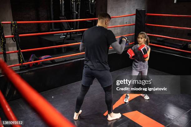 dedicated little girl practicing kickboxing with her male coach in health club - child punching stock pictures, royalty-free photos & images