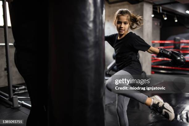 active little caucasian girl kicking the punch bag, while practise boxing - girl punching stock pictures, royalty-free photos & images