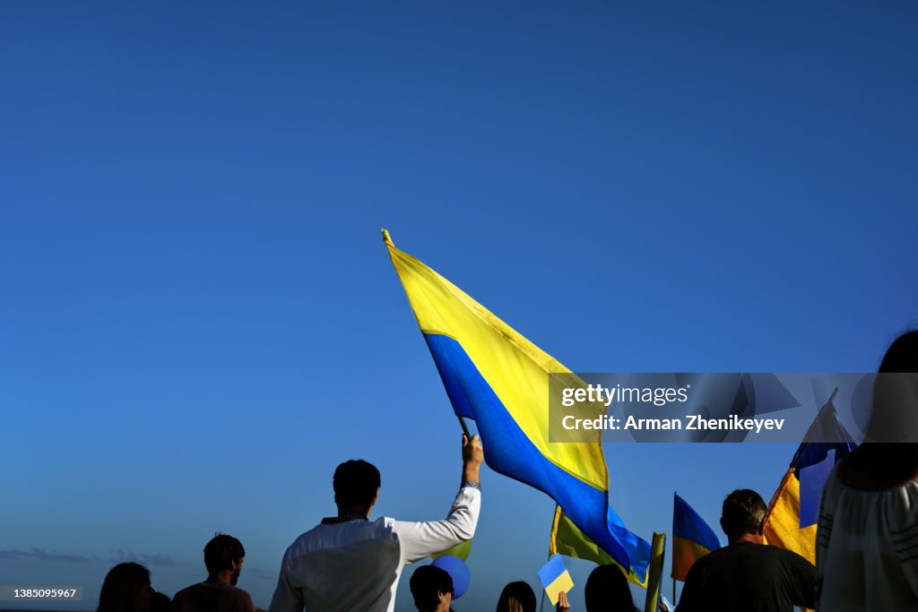 People holding yellow and blue flag of Ukraine in front of the cloudy sky