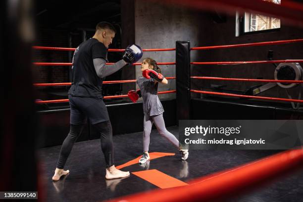 in the boxing ring, little girl practicing kickboxing with her male coach in health club - kid boxing stock pictures, royalty-free photos & images