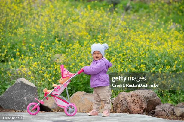 baby child walking with a doll toy trolley outdoors in spring. - baby pram in the park stock pictures, royalty-free photos & images