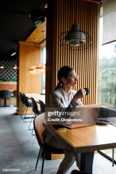 young woman having coffee and using a laptop at a cafe - dress code stock pictures, royalty-free photos & images