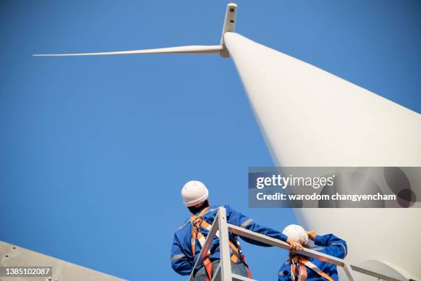 young rope access technicians standing under wind turbine and looking up. - casco de trabajo fotografías e imágenes de stock