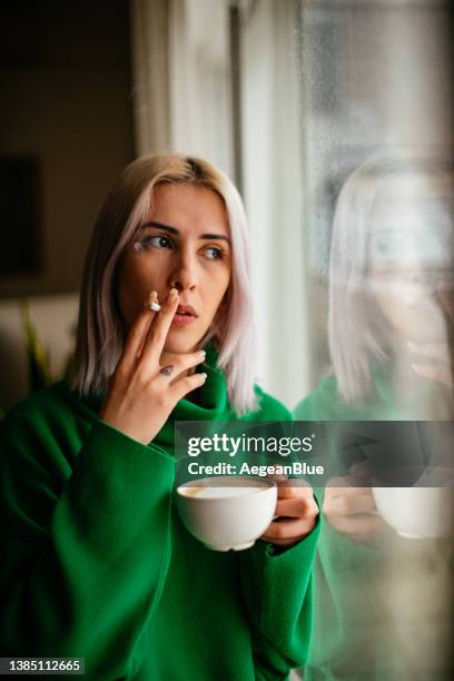 sad woman smoking cigarette in front of window - beautiful women smoking cigarettes stockfoto's en -beelden