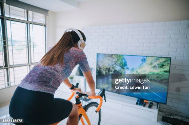 vue arrière femme chinoise asiatique faisant du vélo avec un entraîneur de vélo stationnaire à la maison - bluetooth photos et images de collection