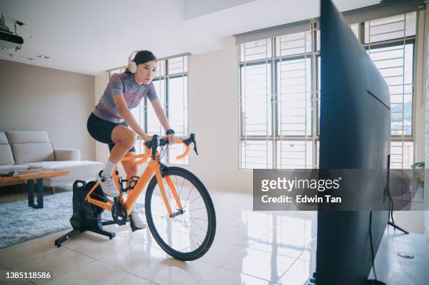 asian chinese woman cycling with stationary bicycle trainer at home - cycling vest stock pictures, royalty-free photos & images