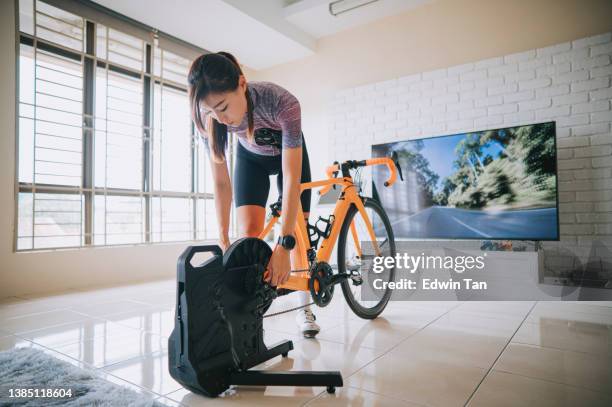 asian chinese woman setting up stationary bicycle trainer at home for routine indoor exercise - home workout stockfoto's en -beelden