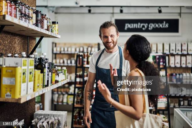 aufnahme eines jungen mannes, der einem kunden hilft, während sie in seinem bioladen einkauft - grocer stock-fotos und bilder