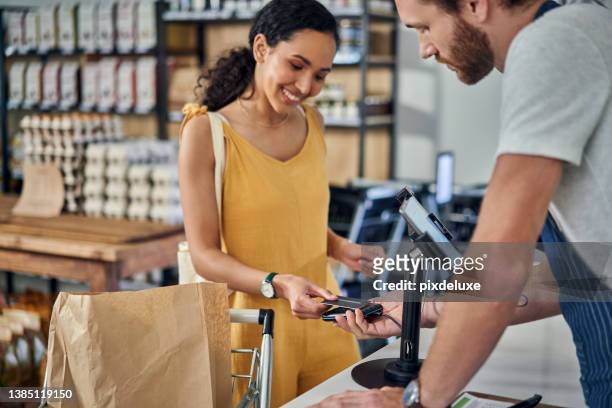 scatto di una giovane donna che paga con una carta di credito in un negozio biologico - paying supermarket foto e immagini stock