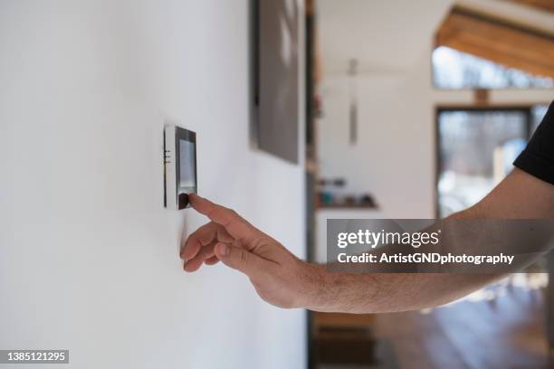 homem em casa ajustando termostato com dispositivo na parede. - thermostat - fotografias e filmes do acervo