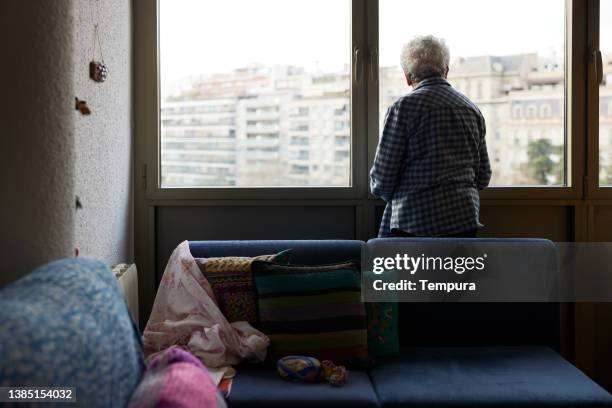 una mujer mayor mirando por la ventana. - una sola mujer mayor fotografías e imágenes de stock