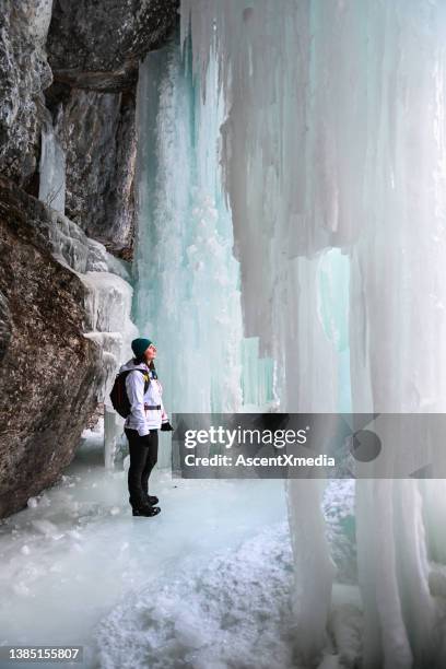 female hiker relaxes under frozen waterfall - frozen waterfall stockfoto's en -beelden