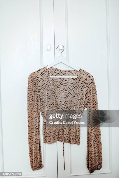 brown polka dot blouse hanging in hanger against white wall - blouse stock pictures, royalty-free photos & images