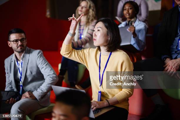 an asian businesswoman attending the conference raises  hand to ask a question - participant stock pictures, royalty-free photos & images