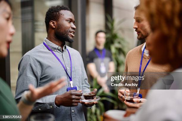 entrepreneurs drinking black coffee while standing with colleagues in convention center - conference center stock pictures, royalty-free photos & images