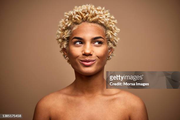 happy african american woman looking away with blonde afro hair style against brown background. - in real life stock-fotos und bilder