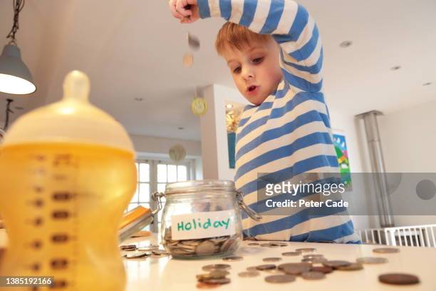 young boy saving money in glass jar - saving up for a rainy day stock pictures, royalty-free photos & images