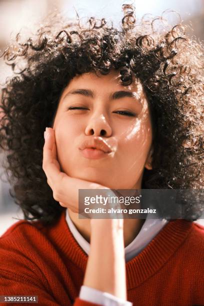 portrait of a woman winking an eye and sending a kiss to the camera while posing outdoors. - blowing a kiss stock pictures, royalty-free photos & images