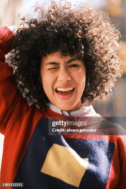 portrait of a young latin woman laughing and winking while posing to the camera outdoors. - augenzwinkern stock-fotos und bilder