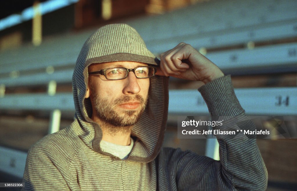 Man with hoodie, hand on glasses, in empty stadium