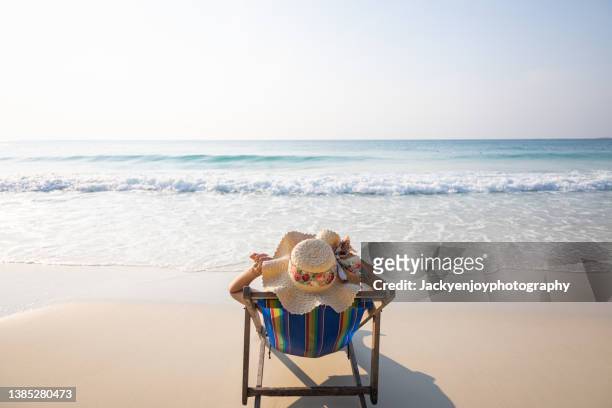 woman relaxing in lawn chair on beach - ligstoel stockfoto's en -beelden
