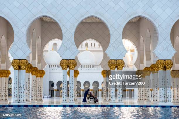 young man pushing a wheel chair in front of abu dhabi mosque - sheikh zayed grand mosque stock pictures, royalty-free photos & images
