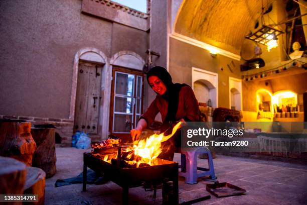 isfahan, iran - april 12, 2016:  young woman firing a fire a pan in a small courtyard in desert - yazd stockfoto's en -beelden