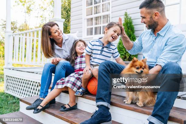 shot of a happy young family of four spending the weekend together at home, standing on the porch with their dog and joking - new deck stock pictures, royalty-free photos & images