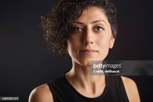 pretty young woman with curly hair  in casual clothing looking at the camera against a dark studio background with copy space - woman short hair serious stock pictures, royalty-free photos & images