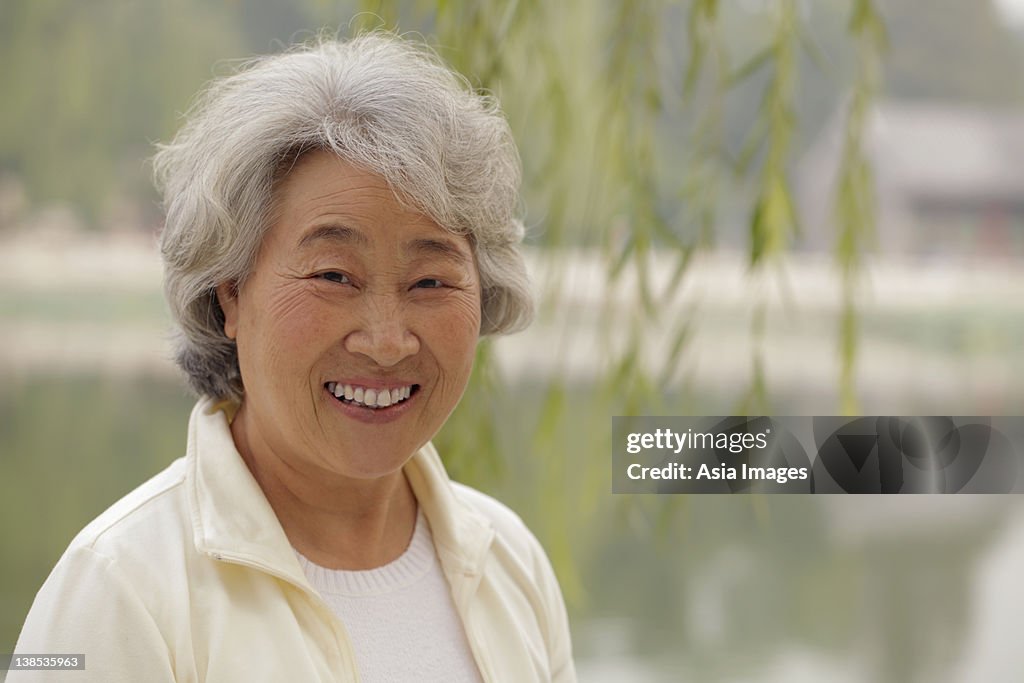 Head shot older woman smiling beneath a tree