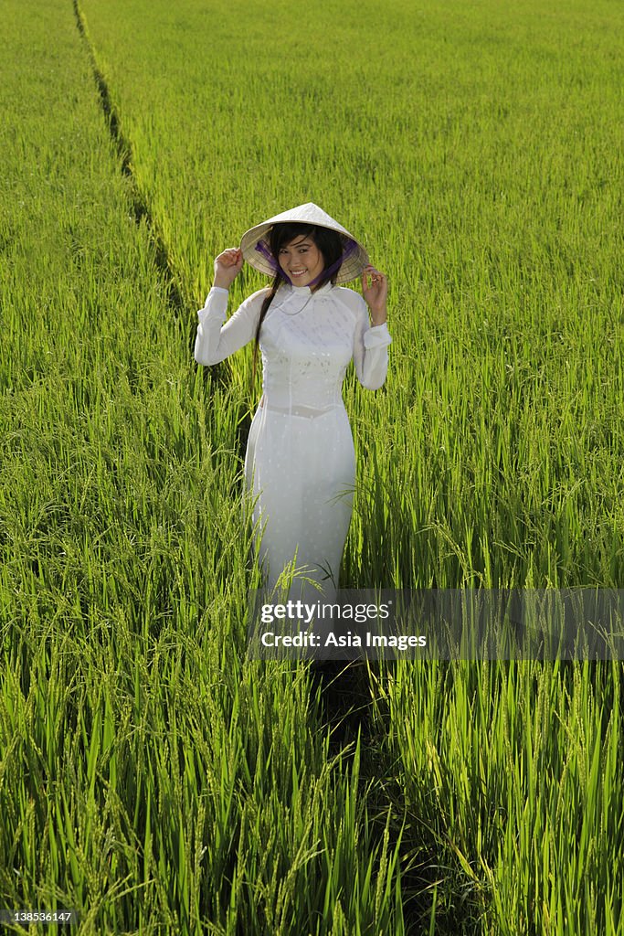 Young woman wearing traditional Vietnamese outfit standing in a rice paddy