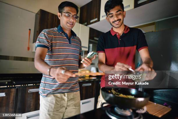 mid adult man and a teenager boy cooking a recipe together in kitchen - boy indian foto e immagini stock