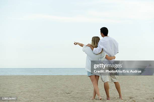 couple walking together at the beach, woman pointing at sea - couple pointing imagens e fotografias de stock