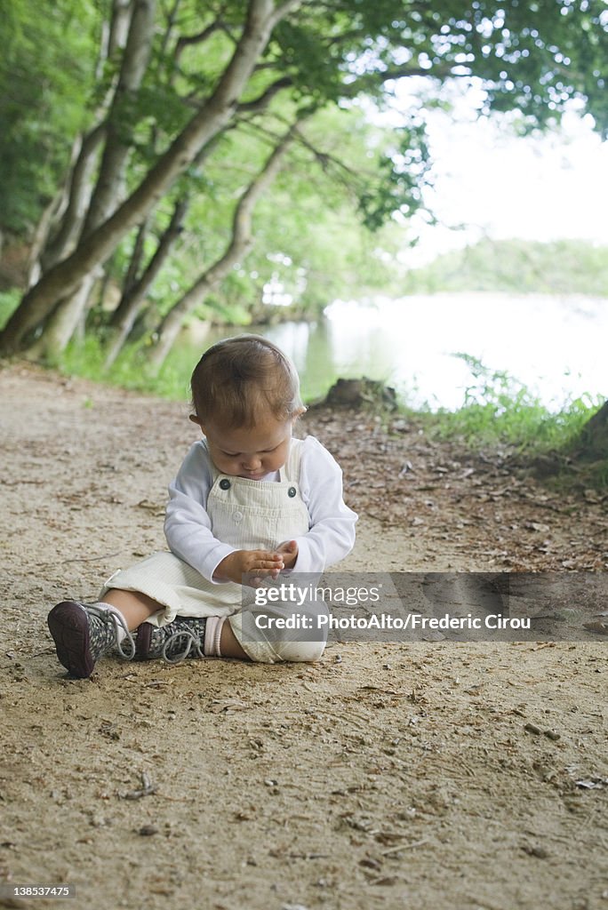 Baby girl sitting on dirt road in woods