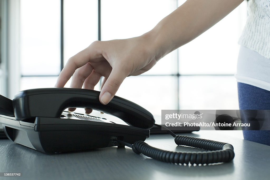 Woman picking up telephone receiver, backlit, cropped