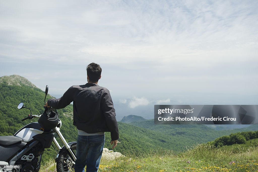 Man standing by motorcycle on mountain, rear view