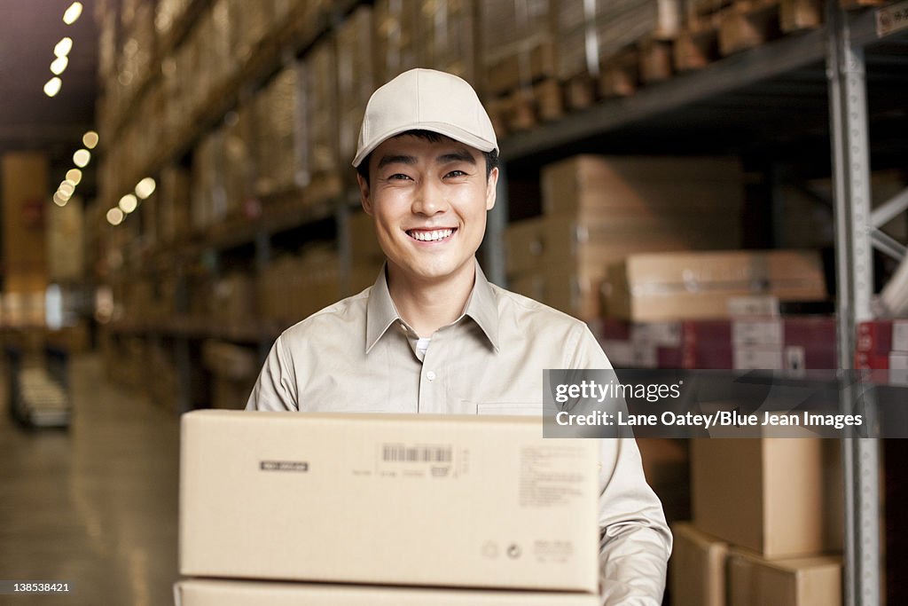 Male Chinese warehouse worker carrying boxes