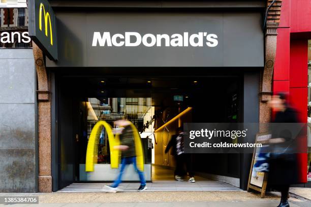 blurred motion of people outside mcdonald's fast food restaurant on city street - mcdonalds restaurant stock pictures, royalty-free photos & images